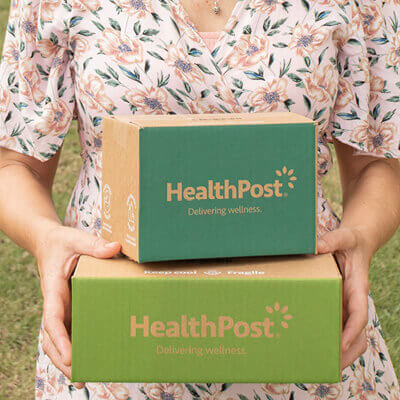 Person holding two HealthPost boxes outdoors.