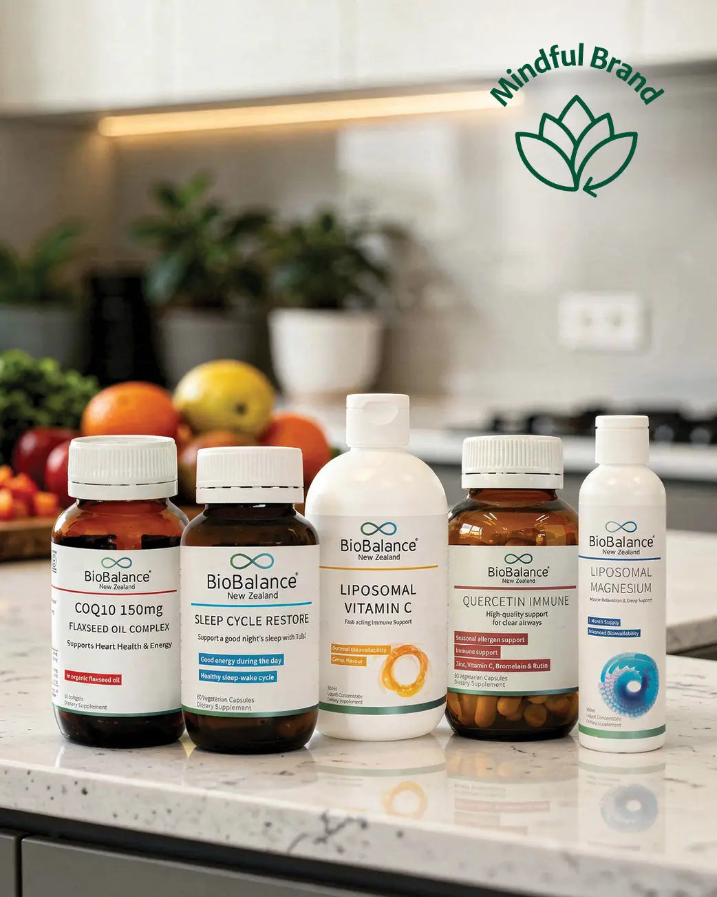 Five BioBalance supplement bottles arranged on a kitchen countertop with blurred fruit and cabinets in the background. The bottles include CoQ10, Sleep Cycle Restore, Liposomal Vitamin C, Quercetin Immune, and Liposomal Magnesium.
