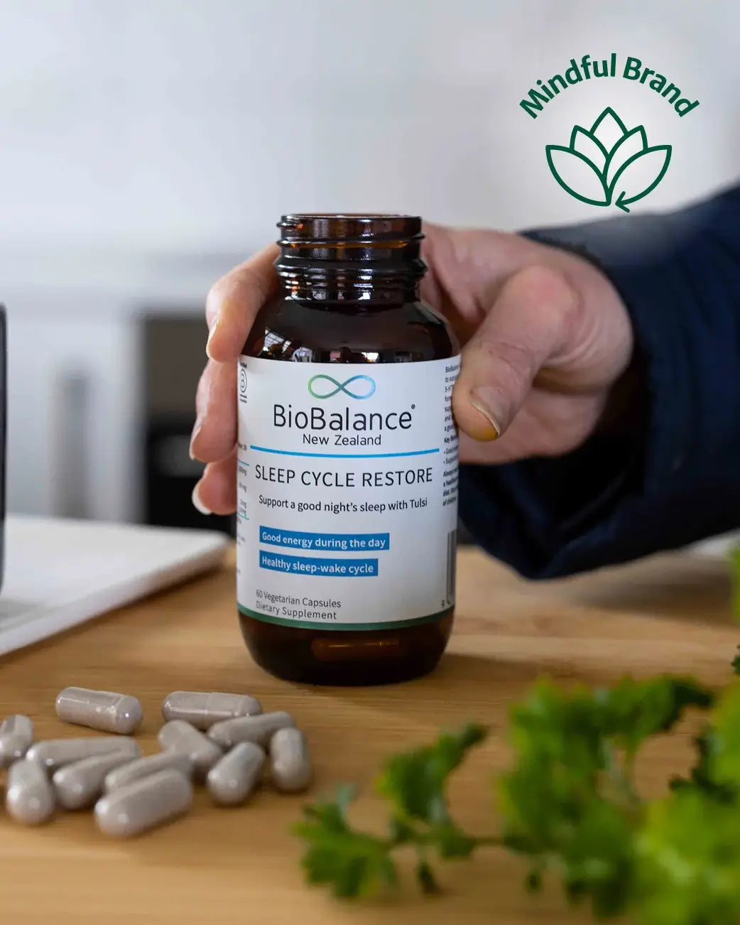 Hand holding a bottle of BioBalance Sleep Cycle Restore supplement with capsules on a wooden surface.