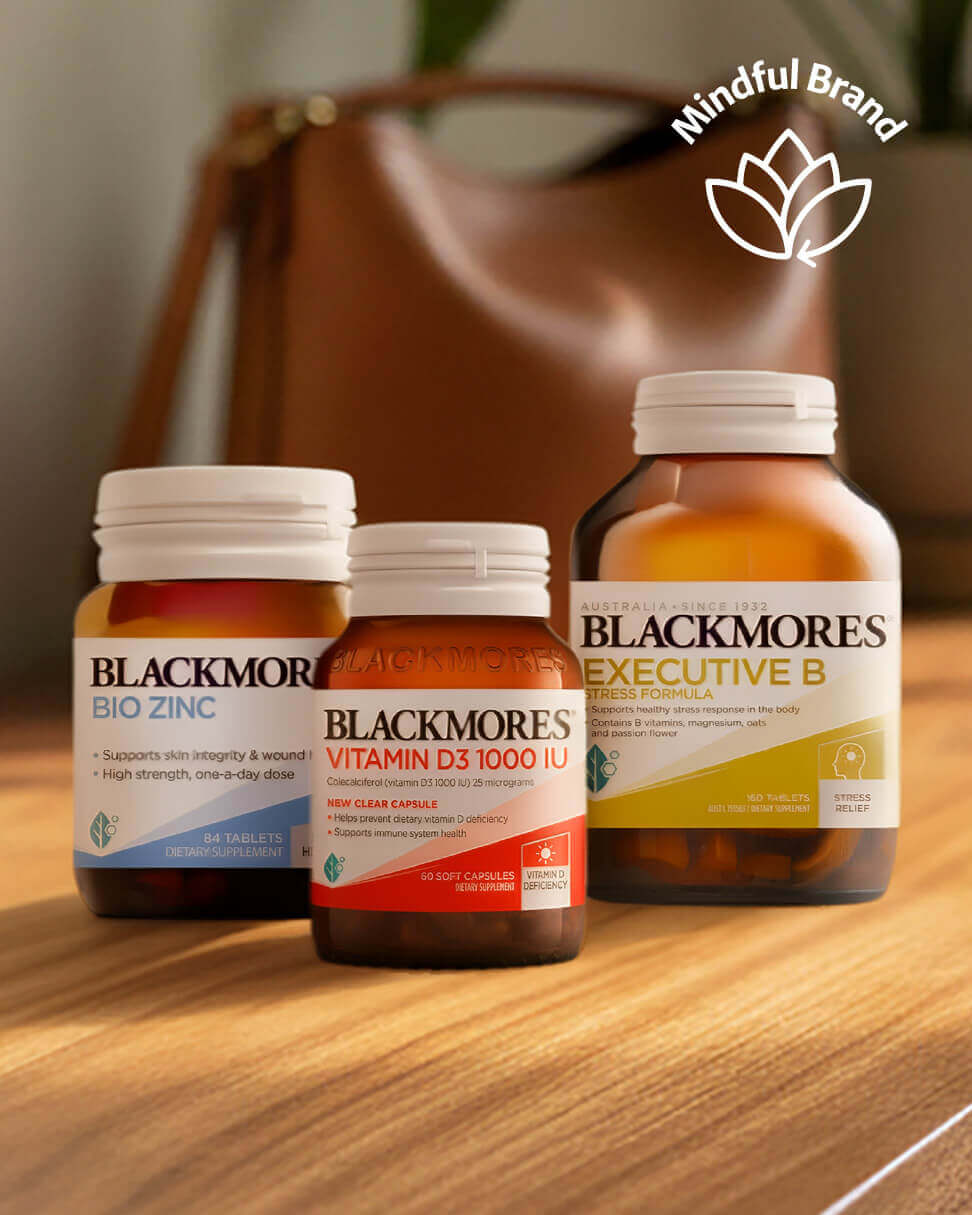 Three Blackmores vitamin bottles on a wooden surface with a blurred brown bag in the background.