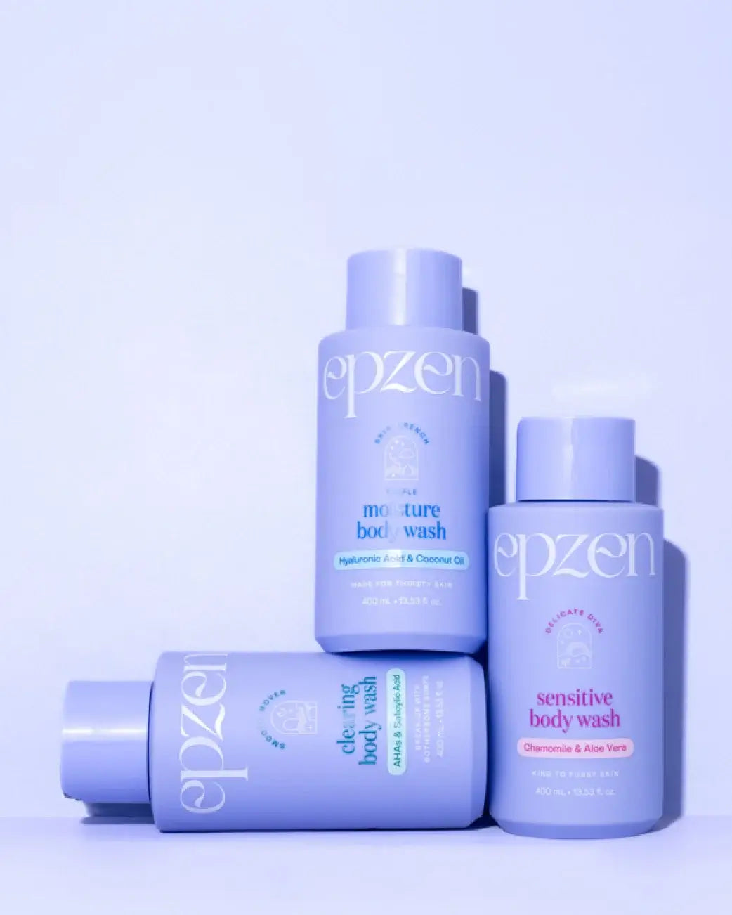 Three lavender-colored Epzen body wash bottles arranged on a light lavender background. One bottle is lying down, and two stand upright.
