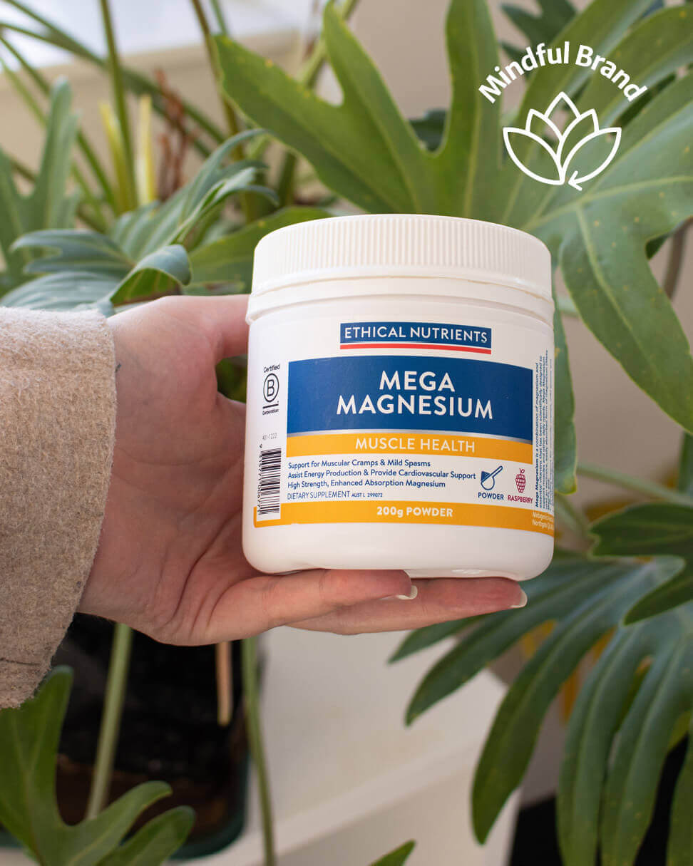 Hand holding a container of Ethical Nutrients Mega Magnesium supplement with plants in the background.