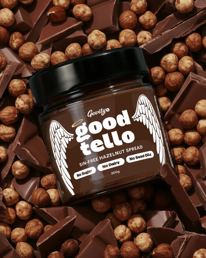 Jar of Goodtello hazelnut spread surrounded by hazelnuts and chocolate pieces.