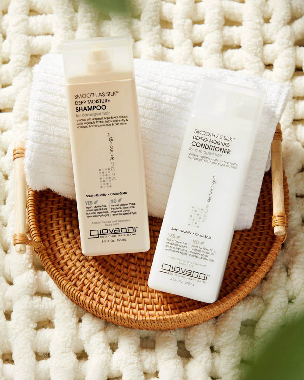 Giovanni shampoo and conditioner bottles on a woven tray with white towels.