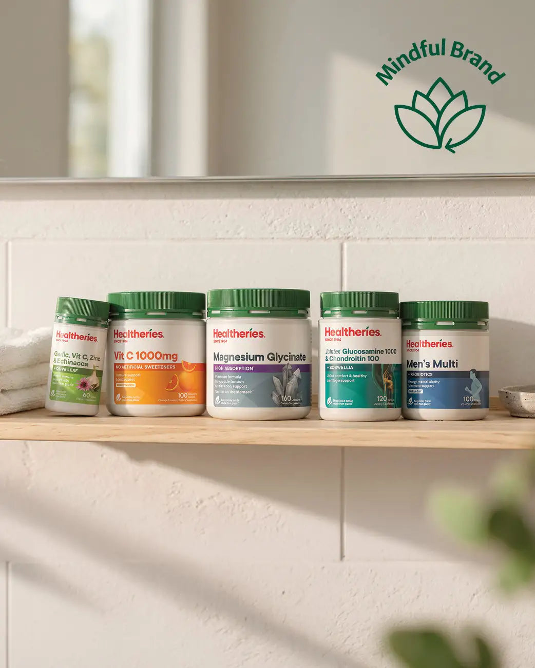 5 popular Healtheries supplements lined up on a wooden shelf underneath a mirror. Green mindful brand logo in the corner.