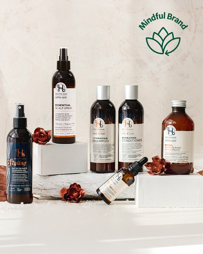 Holistic Hair range staged in a neutral setting with flowers scattered around. Green mindful brand logo in the corner.