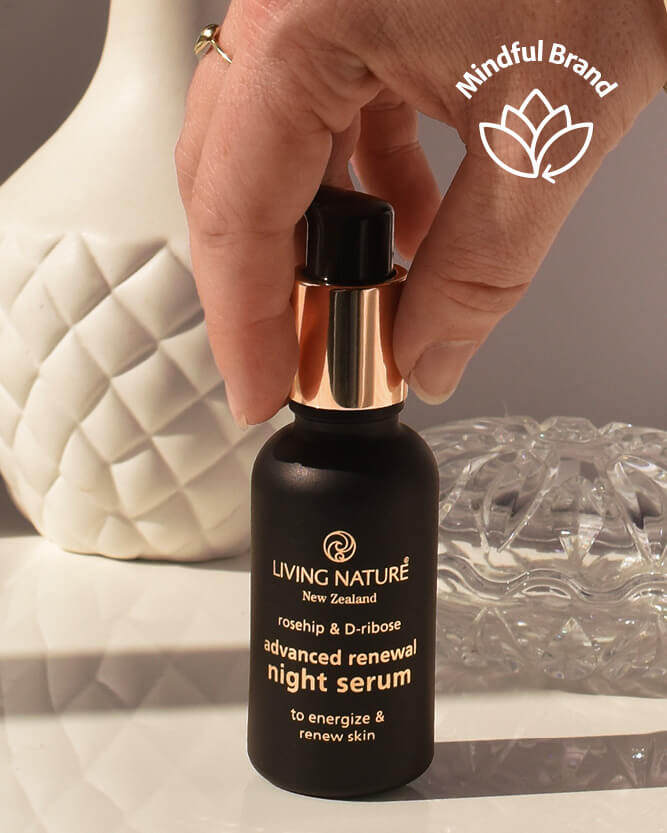 Hand holding a black serum bottle labeled 'Living Nature' with a blurred background.