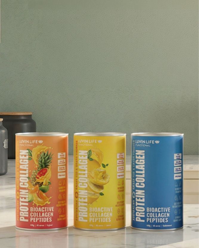 Three tall cylindrical protein collagen powder cans standing on a countertop against a muted green wall. The left can is orange with a pineapple and fruit illustration, the middle can is yellow with citrus slices, and the right can is blue with a white label area.