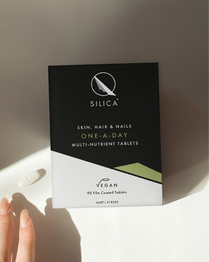 Silica One-A-Day multi-nutrient tablets packaging box, featuring a black and white design with a small green accent, held by a hand on a white surface with soft shadows.