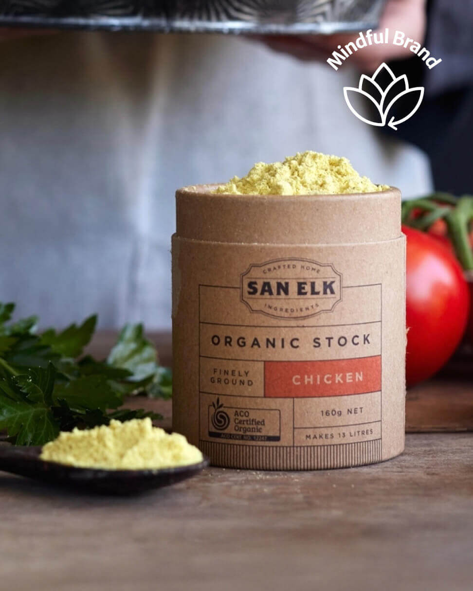 San Elk Organic Stock container with chicken flavor on a wooden surface with vegetables in the background.