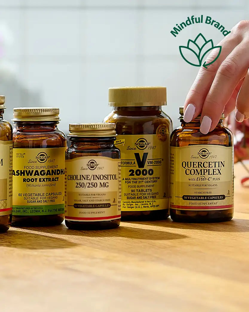 Supplement bottles on a wooden surface with a hand reaching for one bottle, featuring the Mindful Brand logo.
