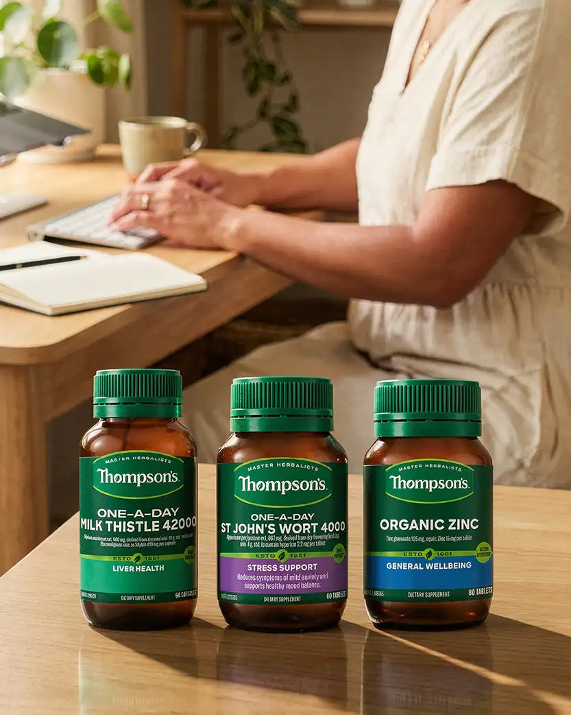 Three Thompsons supplement bottles on a desk with a person working in the background.
