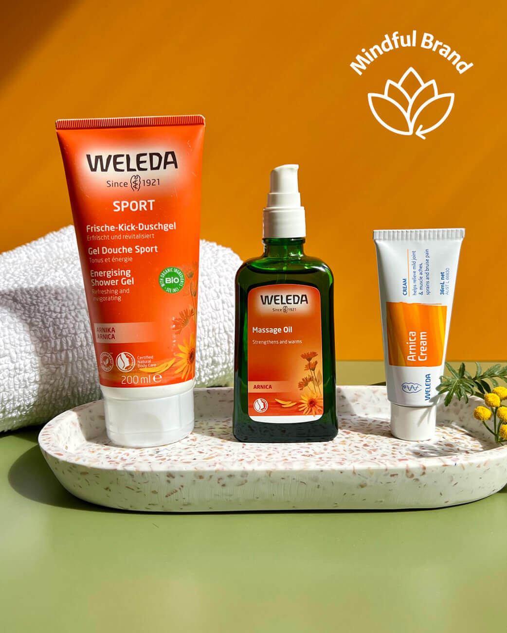 Weleda products including shower gel, massage oil, and cream on a tray with an orange background.