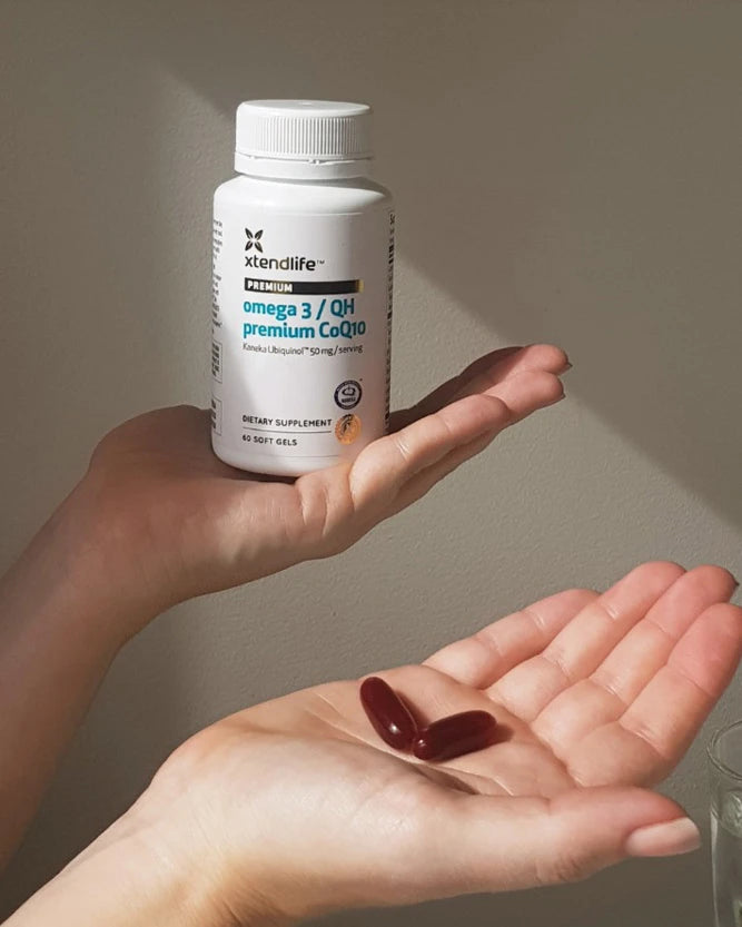 Xtendlife Omega 3 & coQ10 held in a person's hand with large red softgels in the other hand.