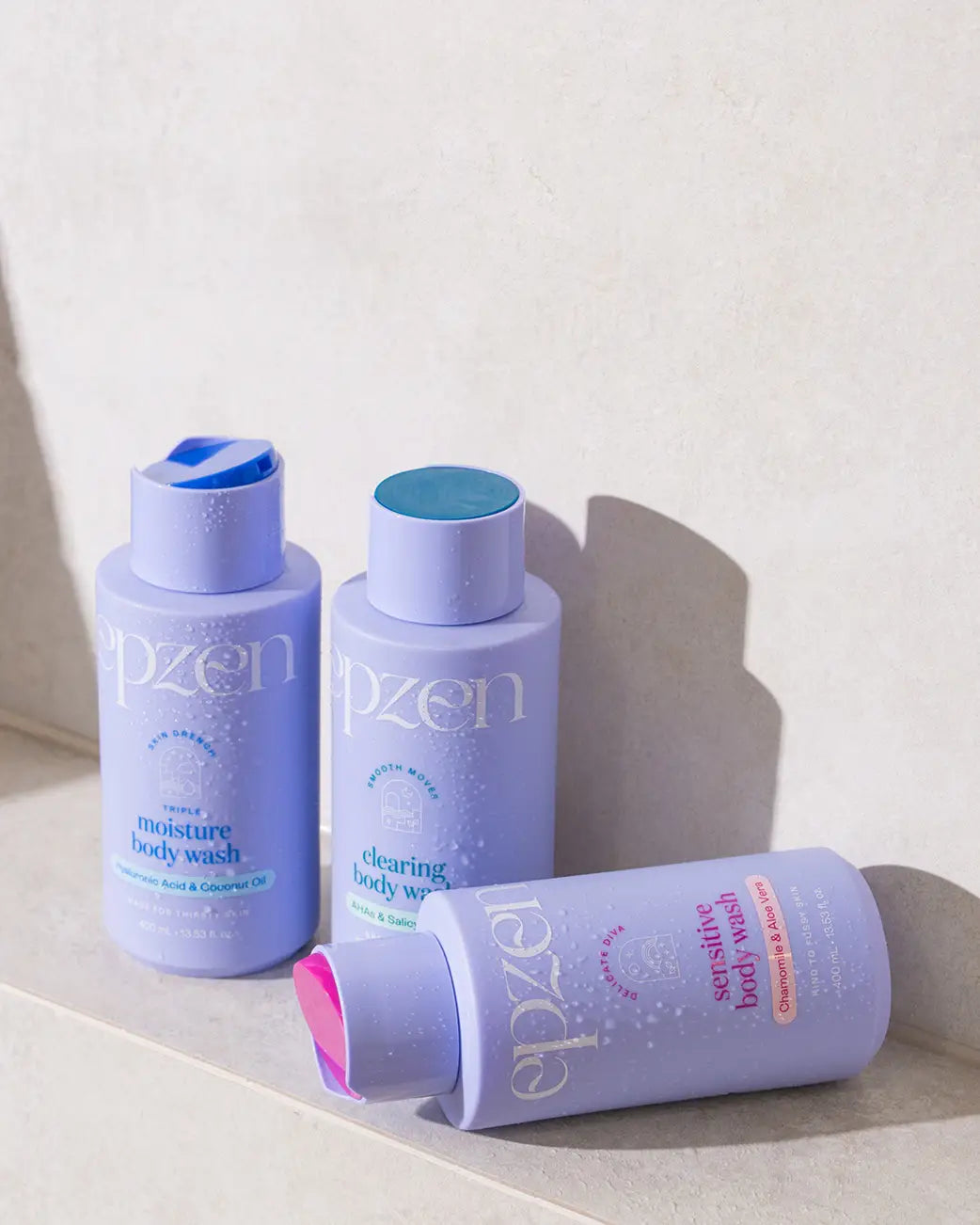 3 purple bottles of epzen body wash arranged on a beige shower ledge.