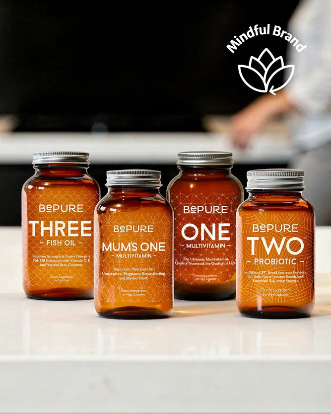 Four amber supplement bottles labeled B&PURE Three Fish Oil, Mums One Multivitamin, One Multivitamin, and Two Probiotic, arranged on a white countertop with a blurred kitchen background and a 'Mindful Brand' logo in the top right.