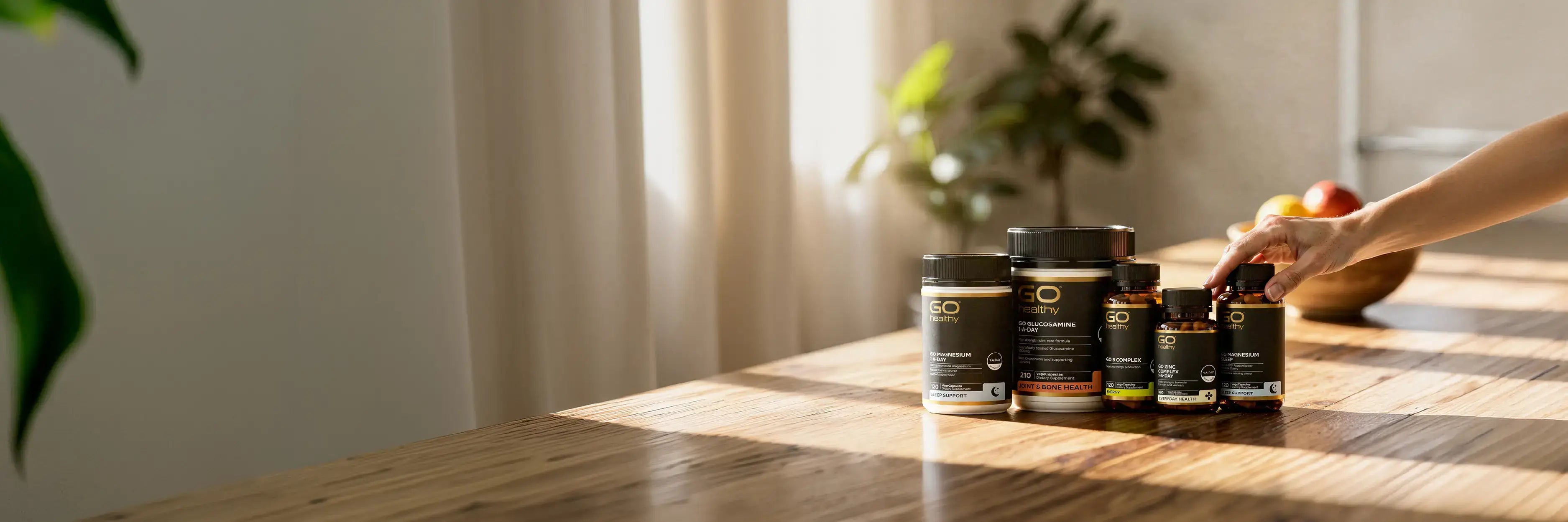 Hand picking GO Healthy supplement products on a wooden table.