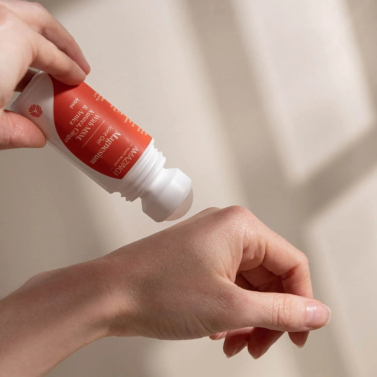Person applying Magnesium joint gel roll-on to their hand with a beige background.