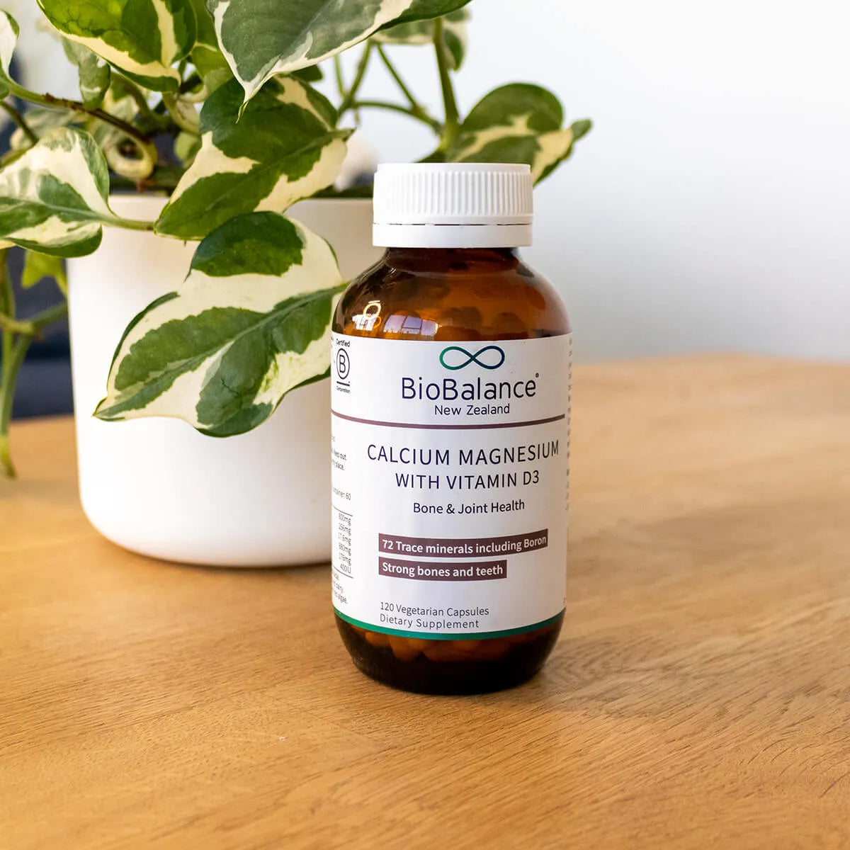 BioBalance calcium magnesium with vitamin D3 supplement bottle on a wooden surface with a plant in the background.