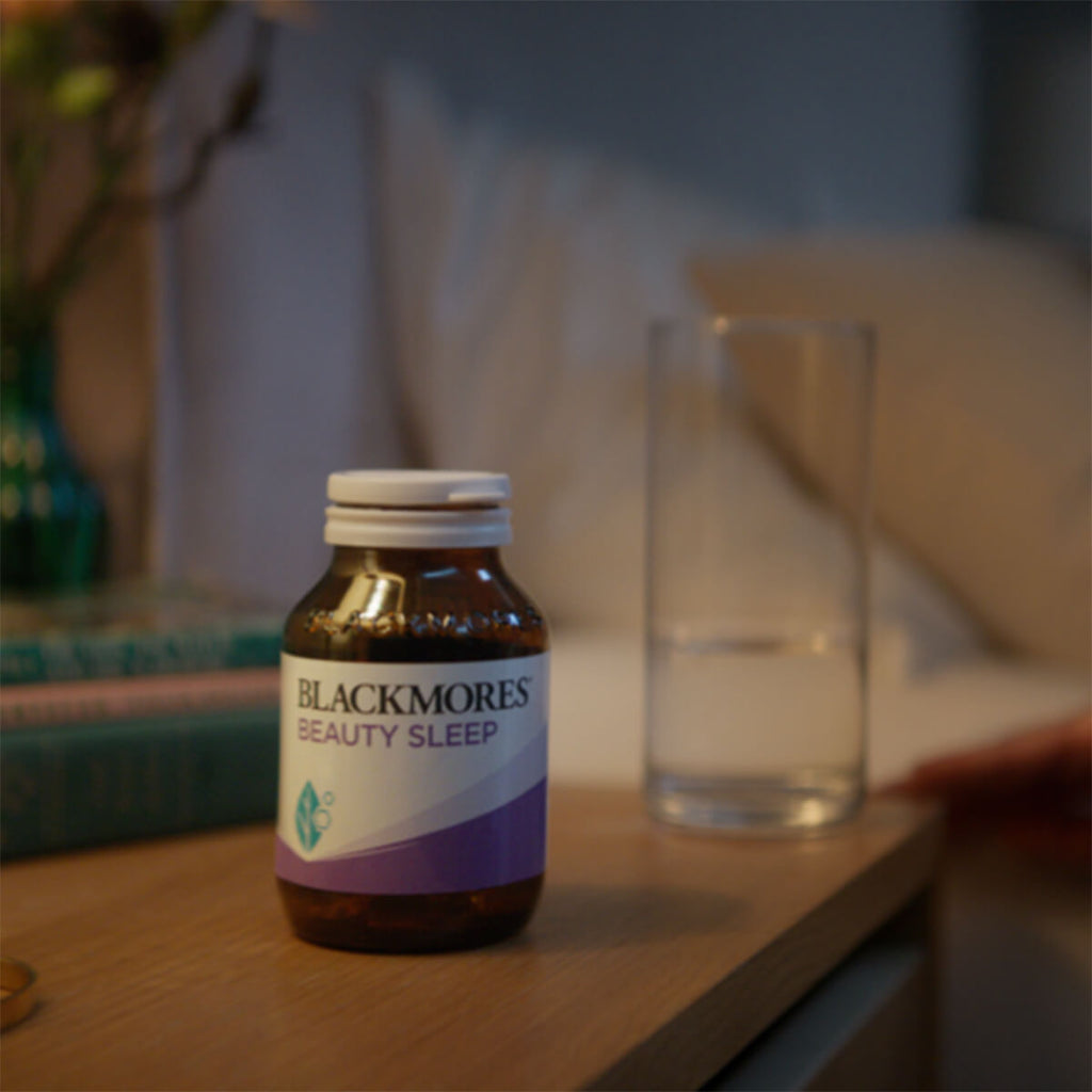 Blackmores Beauty Sleep supplement bottle on a table with a glass in the background.
