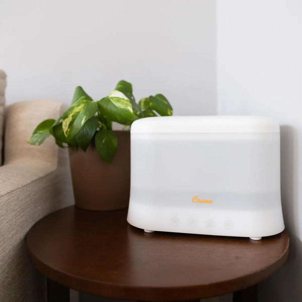 White plastic rectangular humidifier and aroma diffuser on a round wooden table next to a plant.