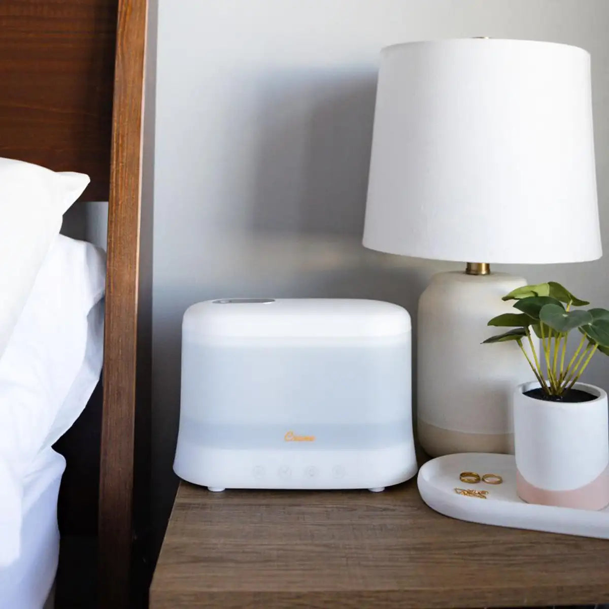 White plastic rectangular humidifier and aroma diffuser on a wooden bedside table next to a lamp.