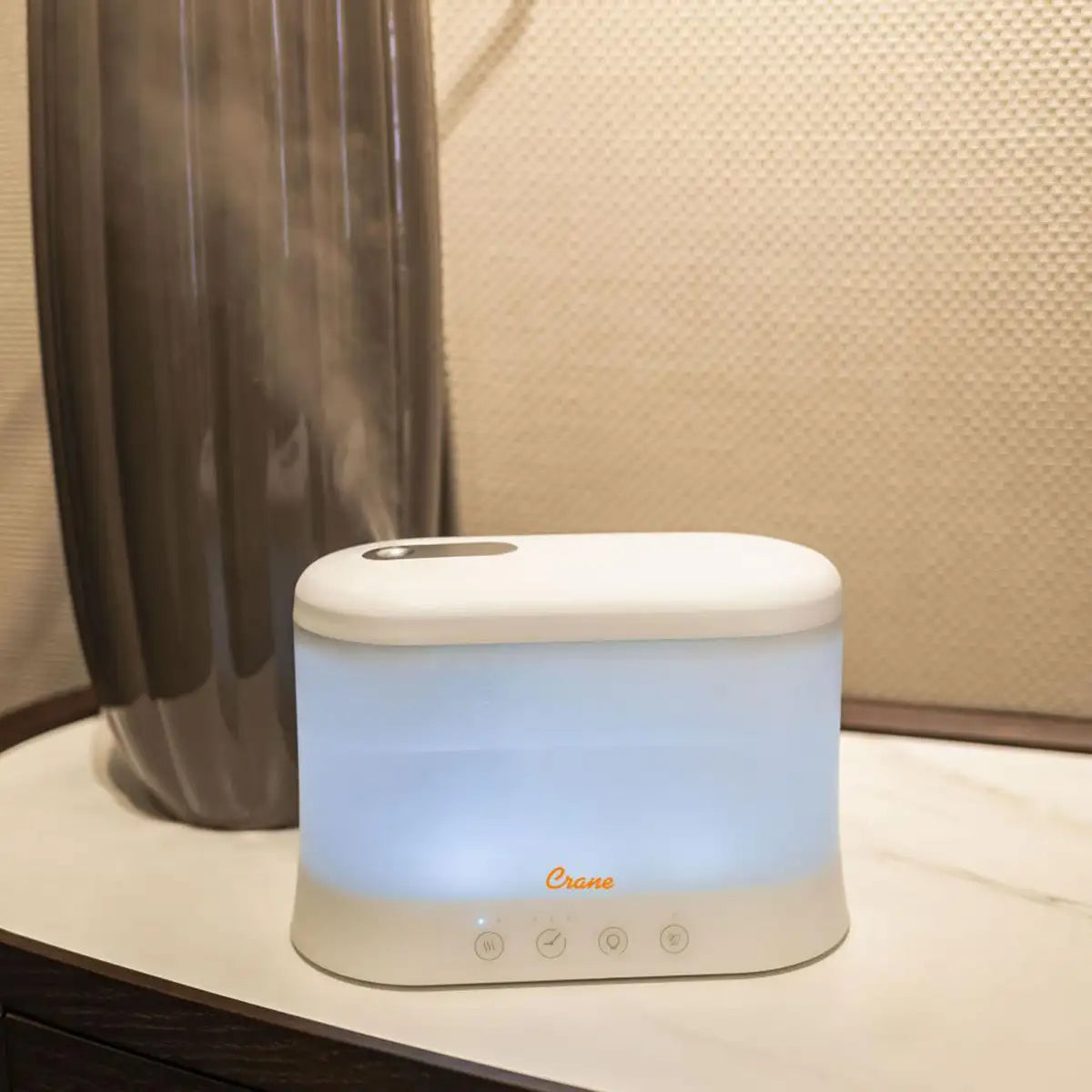 White plastic rectangular humidifier and aroma diffuser with the light on, placed on a white counter against a beige wall.