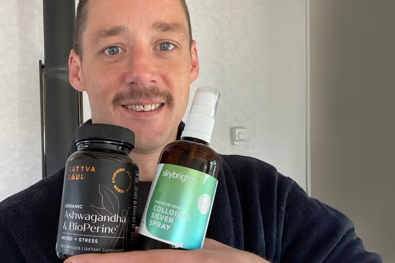 man holding two supplement bottles in front of cream wall
