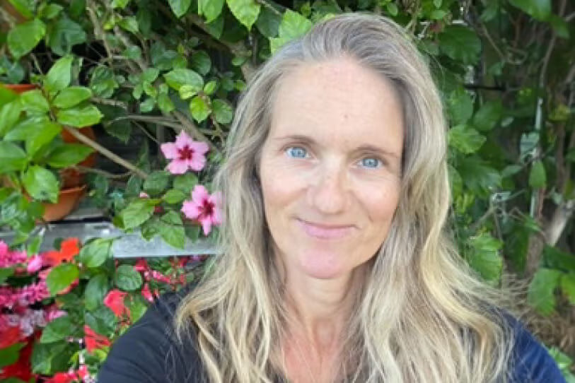 woman with long hair standing in front of green trees and pink flowers 