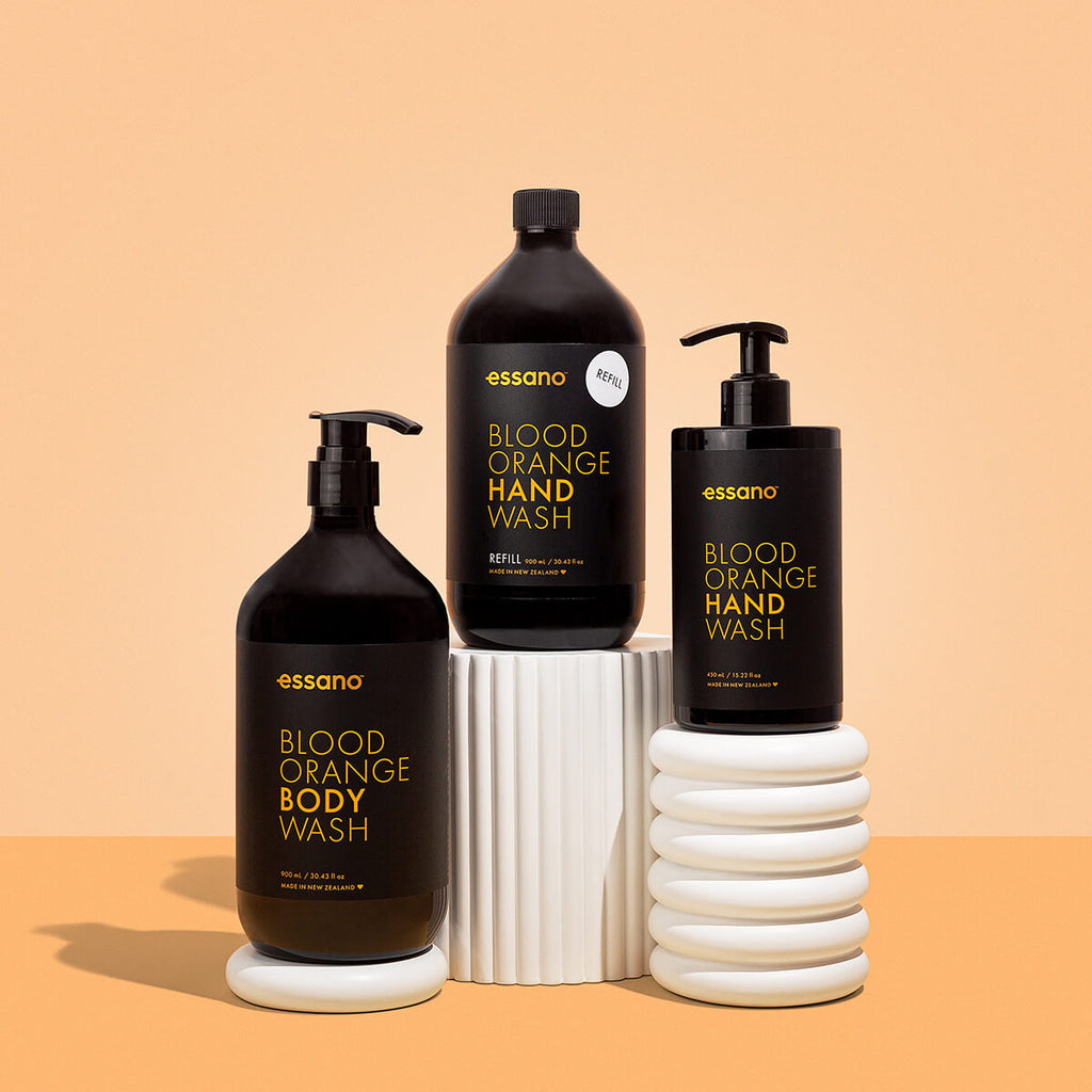 Three bottles of essano Blood Orange Hand Wash, Body Wash, and Refill on a beige background.