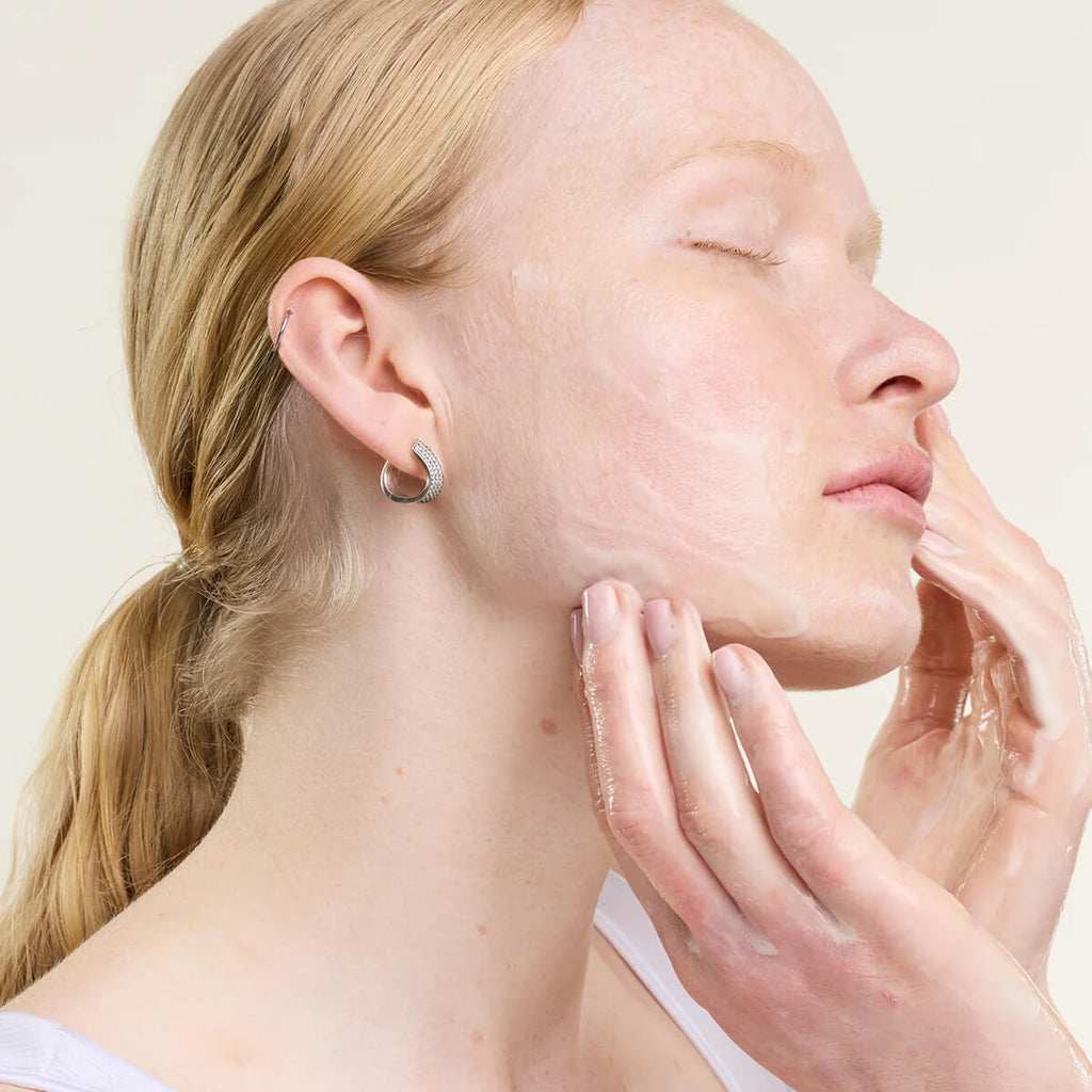 Woman touching her face with a neutral background.