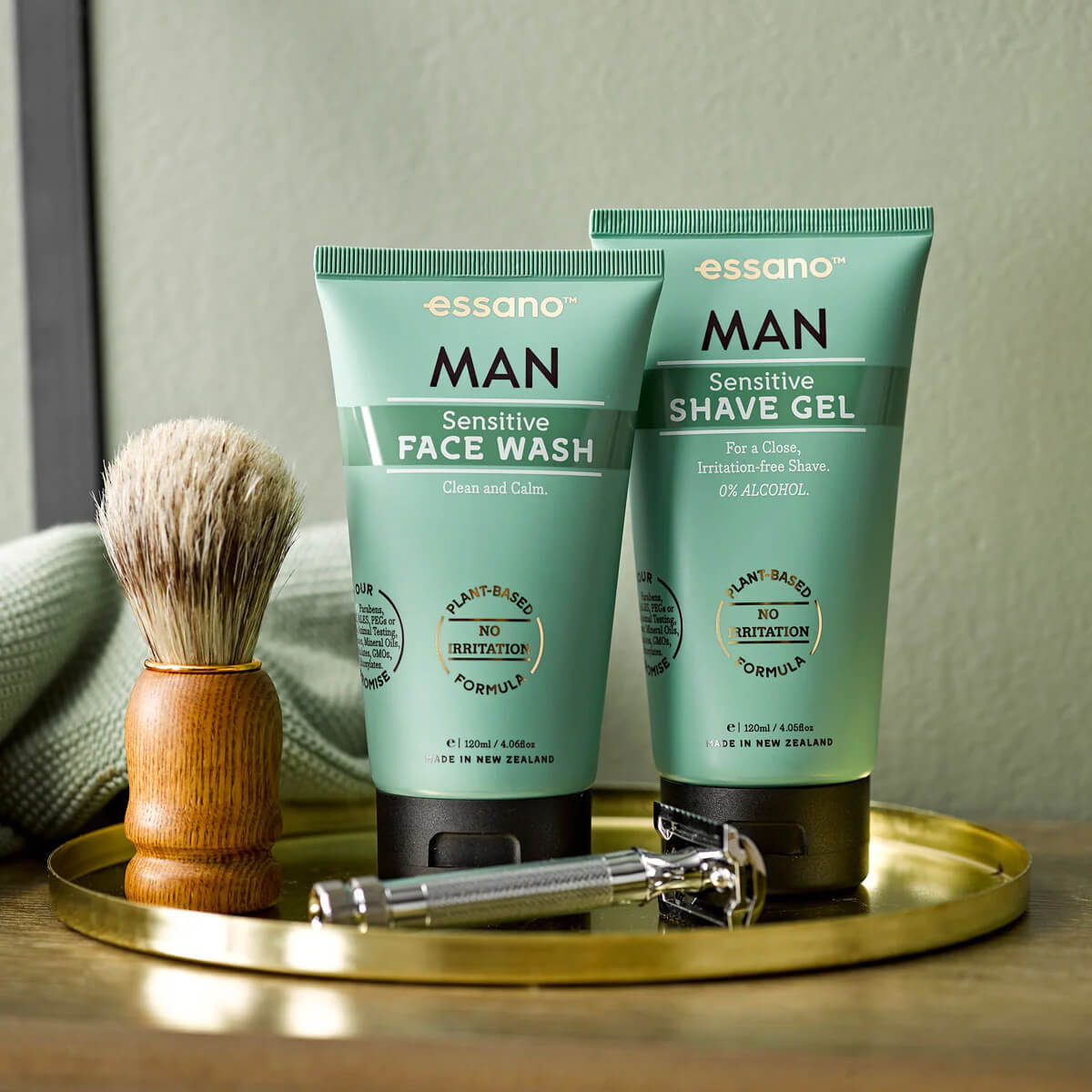 Two tubes of essano Man Sensitive Face Wash and Shave Gel on a gold tray with a wooden brush and razor.