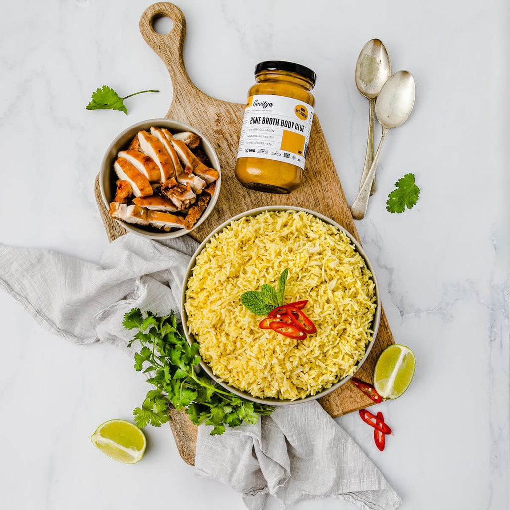 Bowl of yellow rice with chicken, a jar of curry sauce, and garnishes on a marble surface.