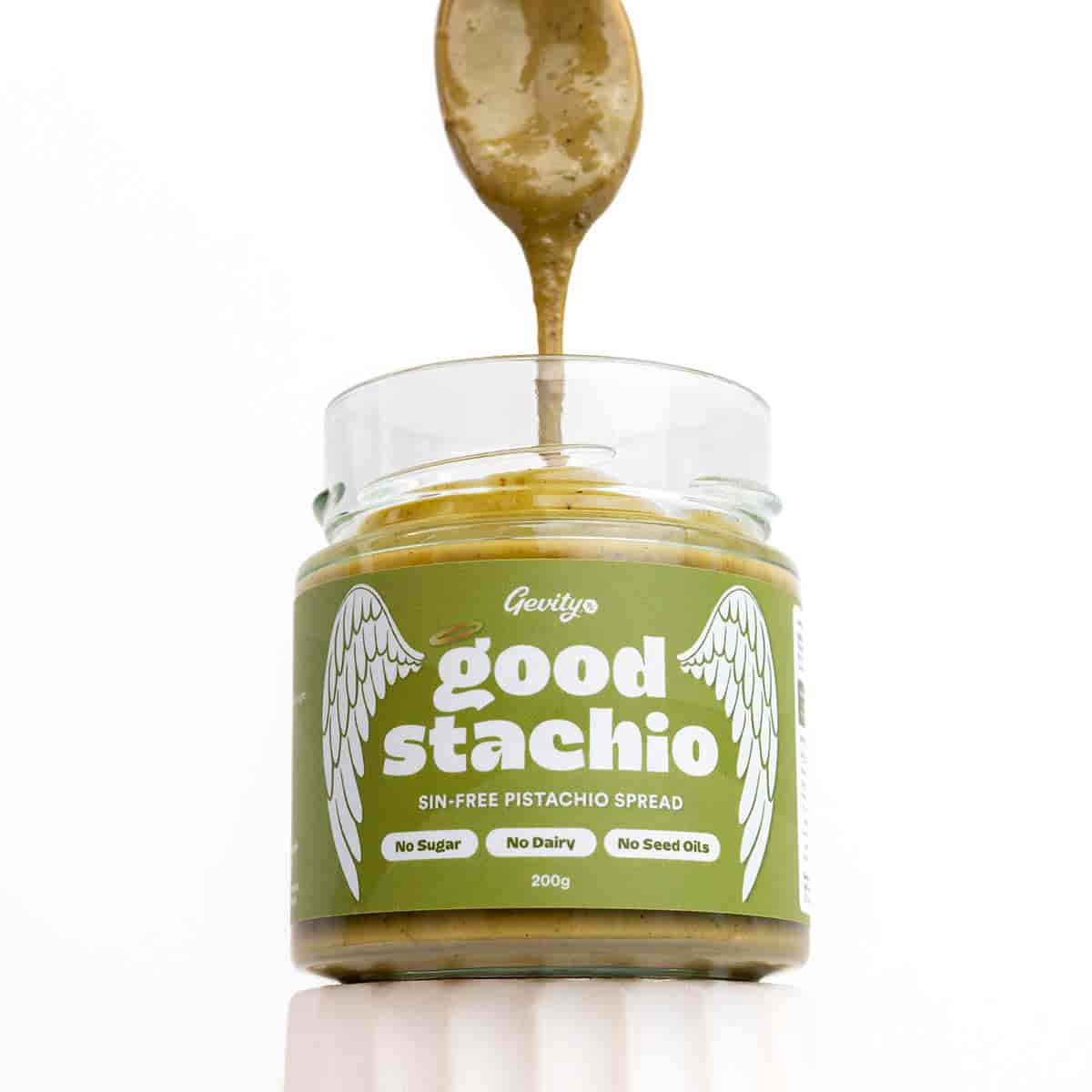 Jar of 'good stachio' pistachio spread with a spoonful being lifted out, on a white background.