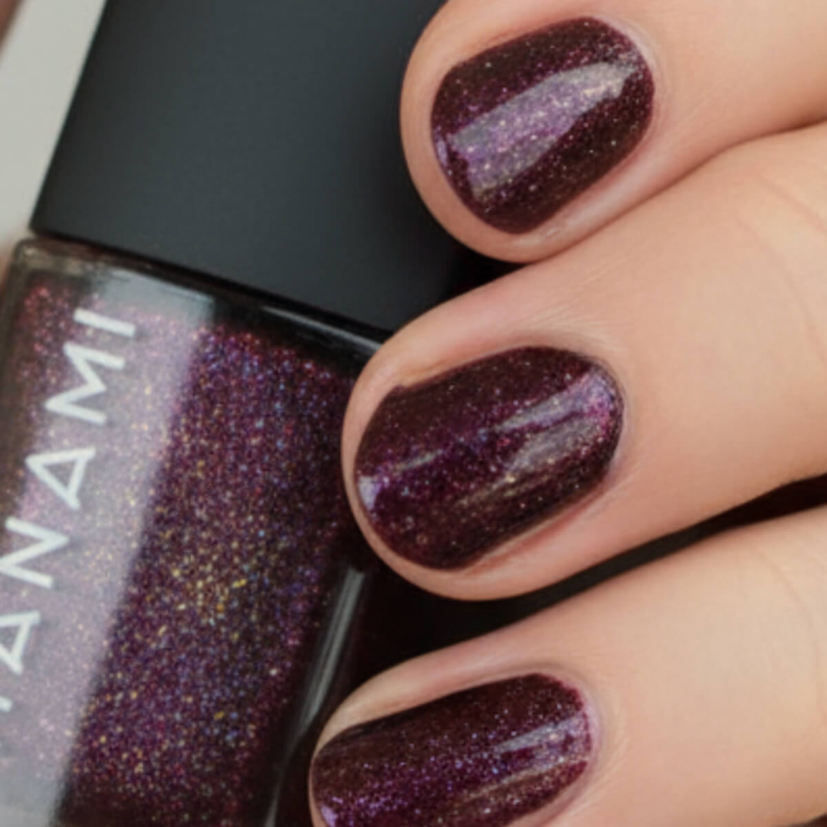 Close-up of hands with dark glittery nail polish and a bottle of Hanami nail polish.
