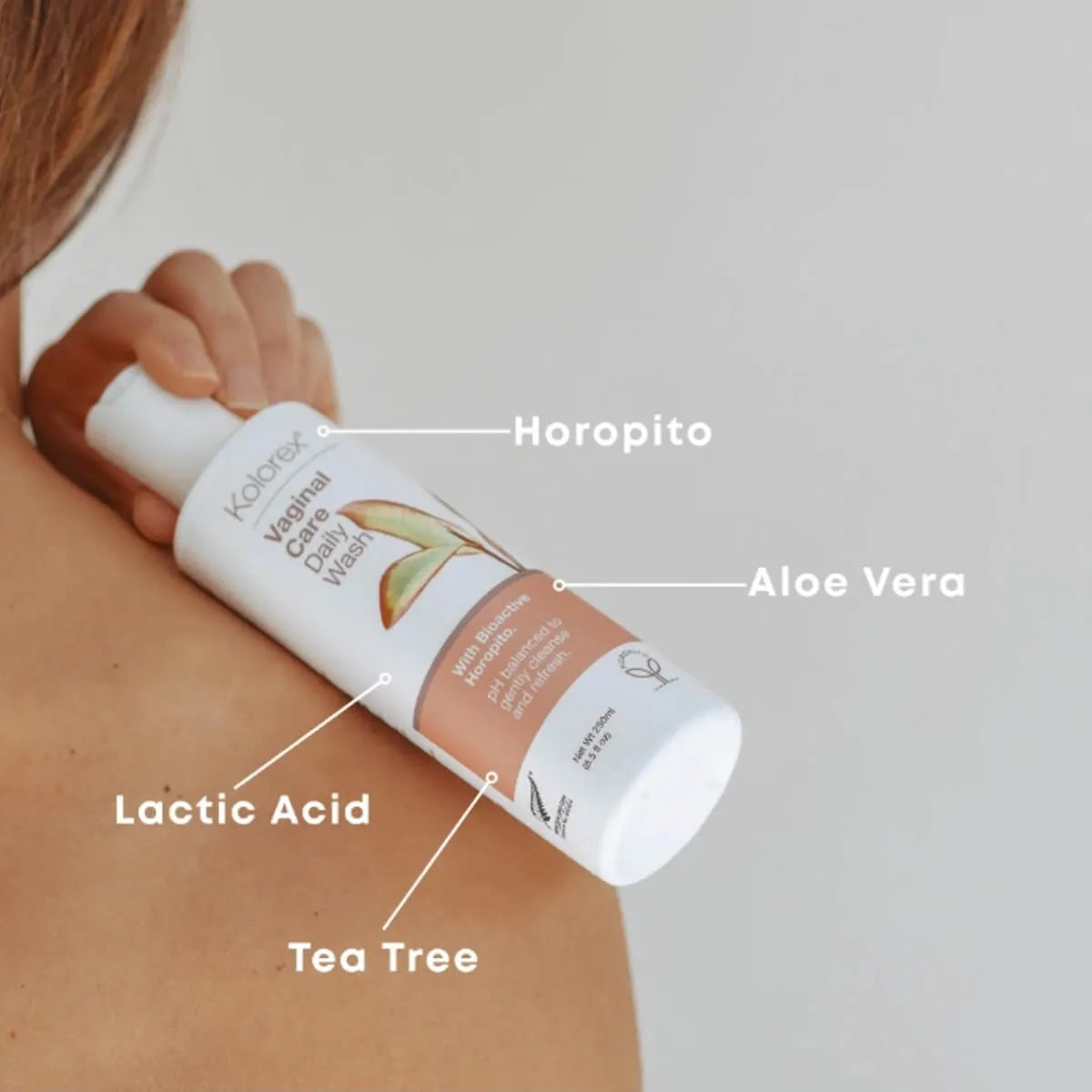 Person holding intimate wash product labelled with ingredients on a neutral background.