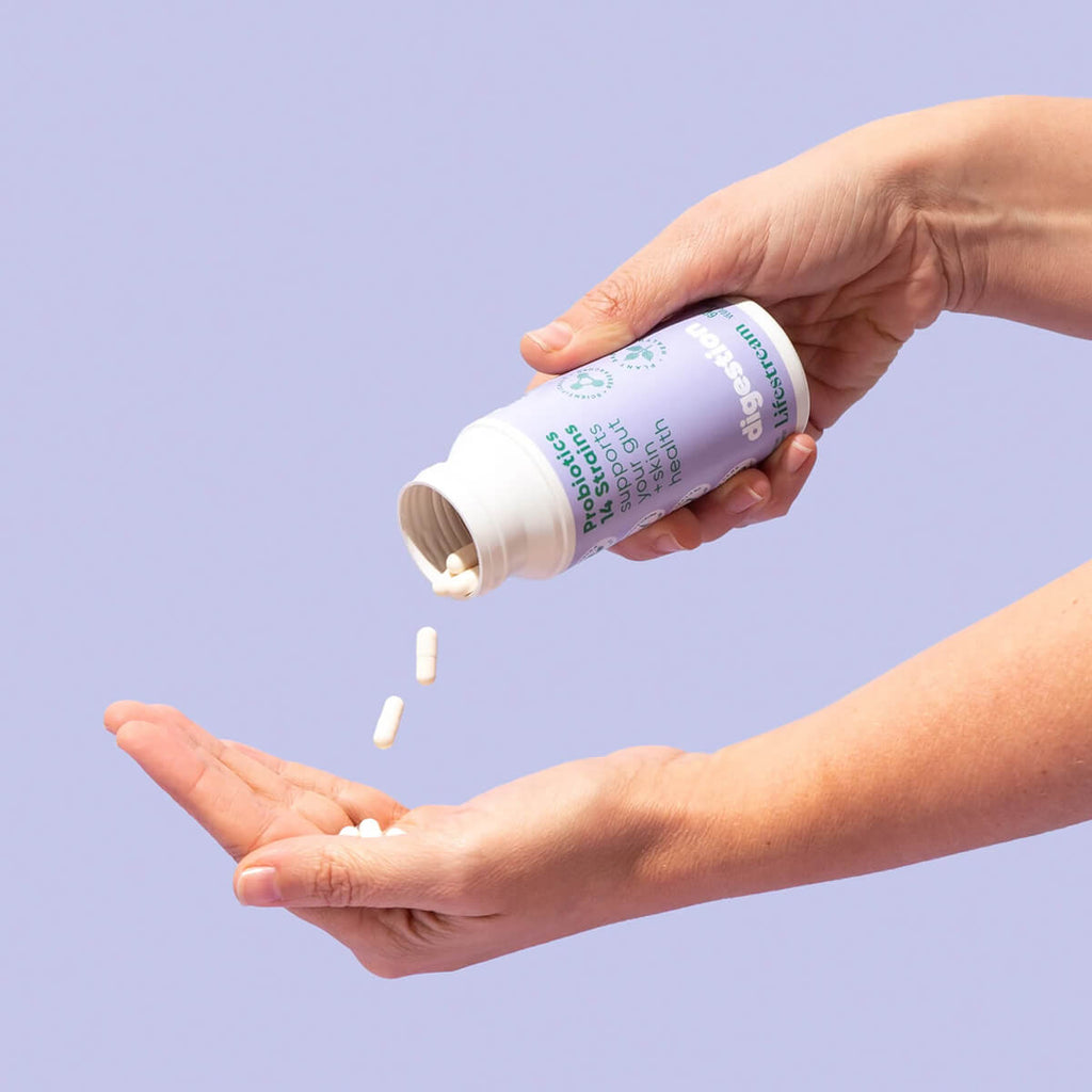 Person pouring supplements from a bottle into their hand against a light purple background.