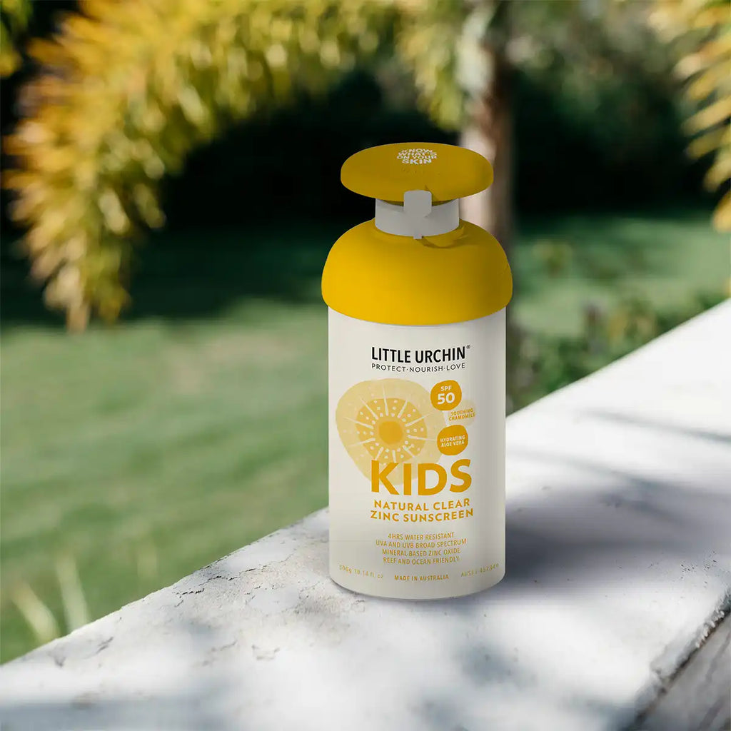 Little Urchin kids sunscreen pump bottle on a stone ledge with greenery in the background.
