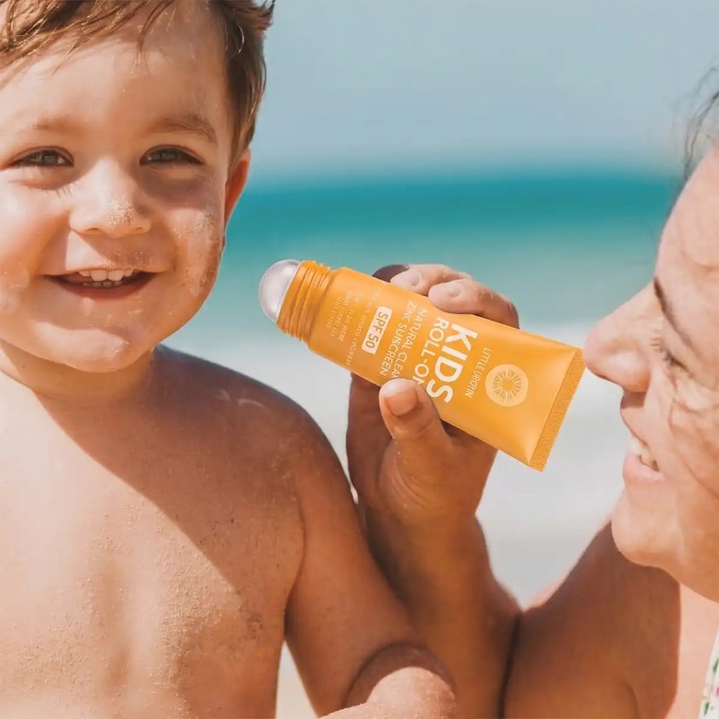 A child on a beach holding an orange sunscreen bottle with an adult beside them.