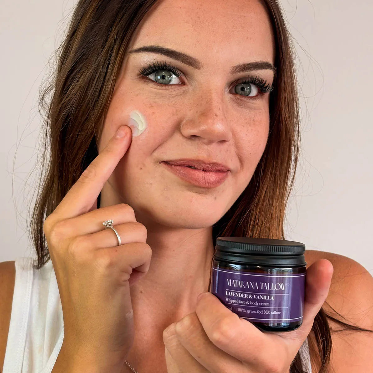 Woman applying cream to her face with a jar of Lavender Vanilla tallow cream.