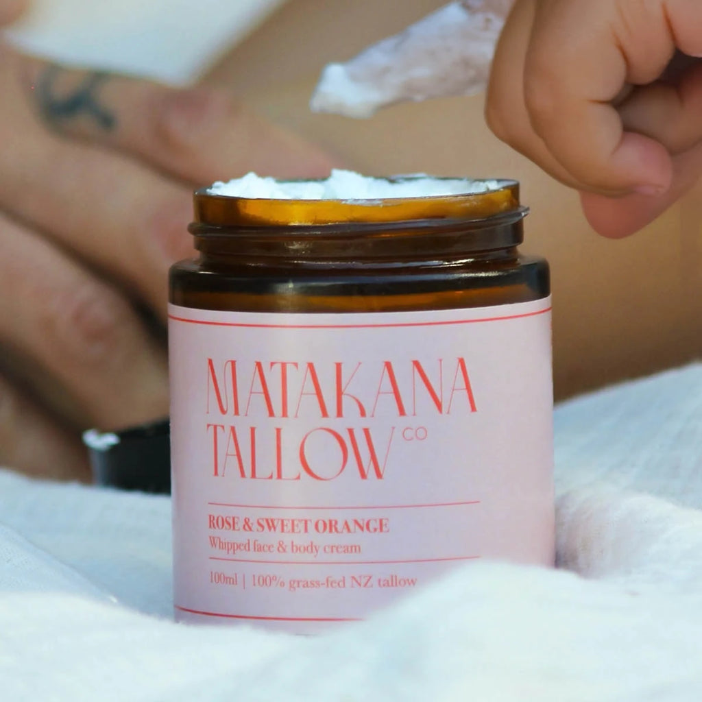 Matakana Tallow cream jar with a hand applying cream on a white surface