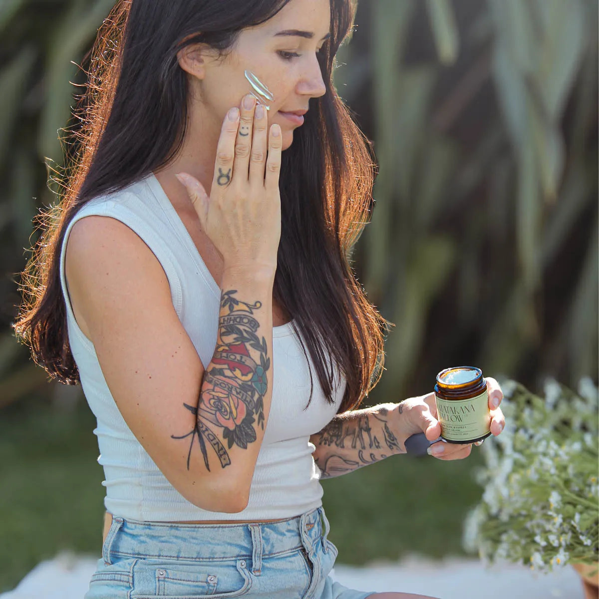 Woman applying tallow cream to her face outdoors with a jar of cream in her hand.