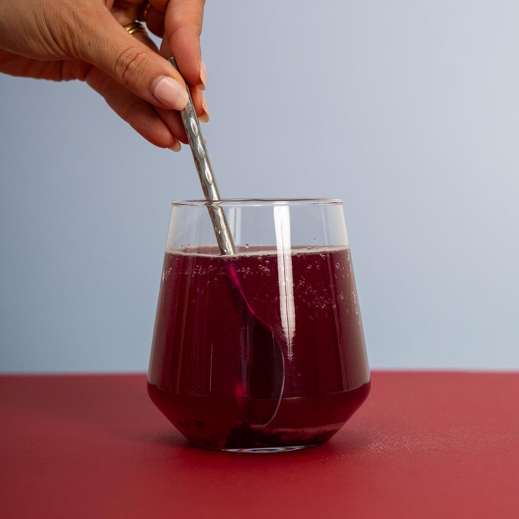Glass of red blood sugar sync with a spoon being stirred, on a red surface with a light blue background