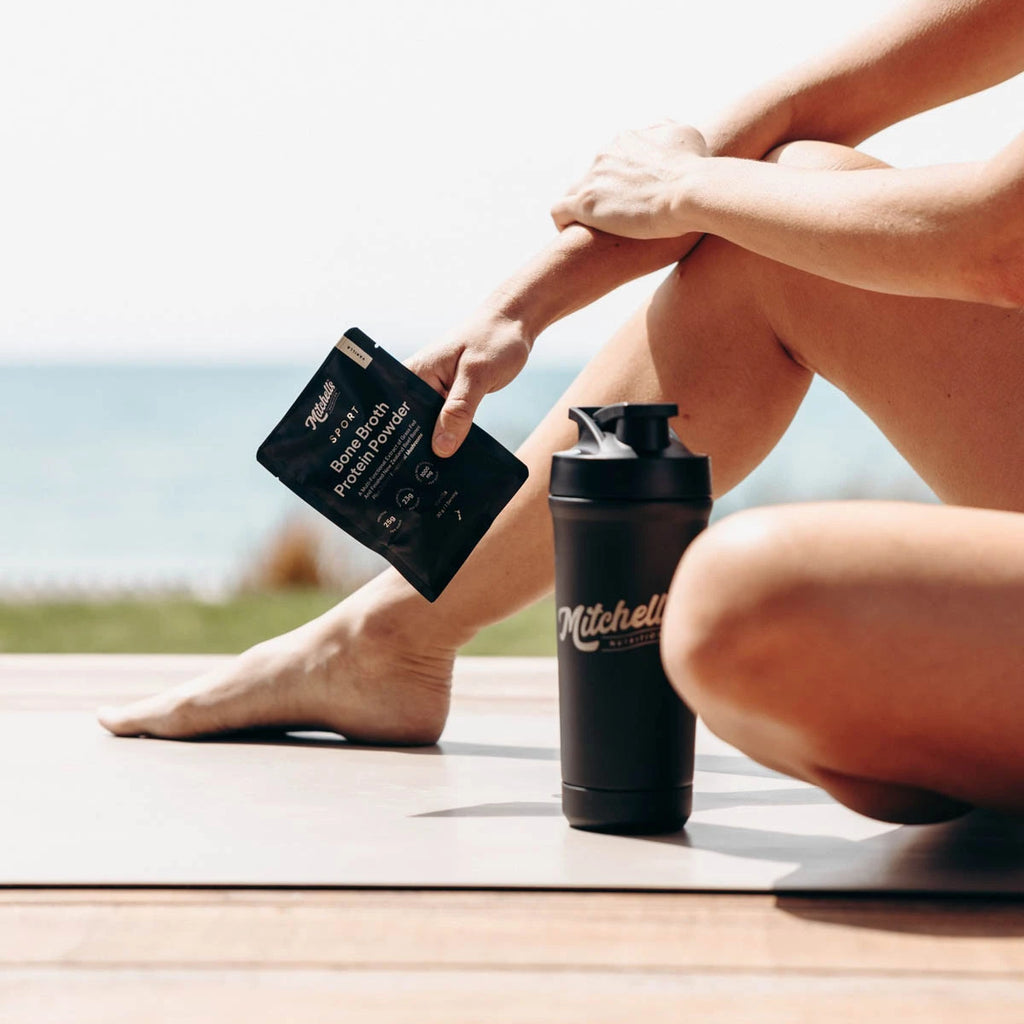 Person sitting on a wooden deck with a shaker and supplement packet, outdoors.