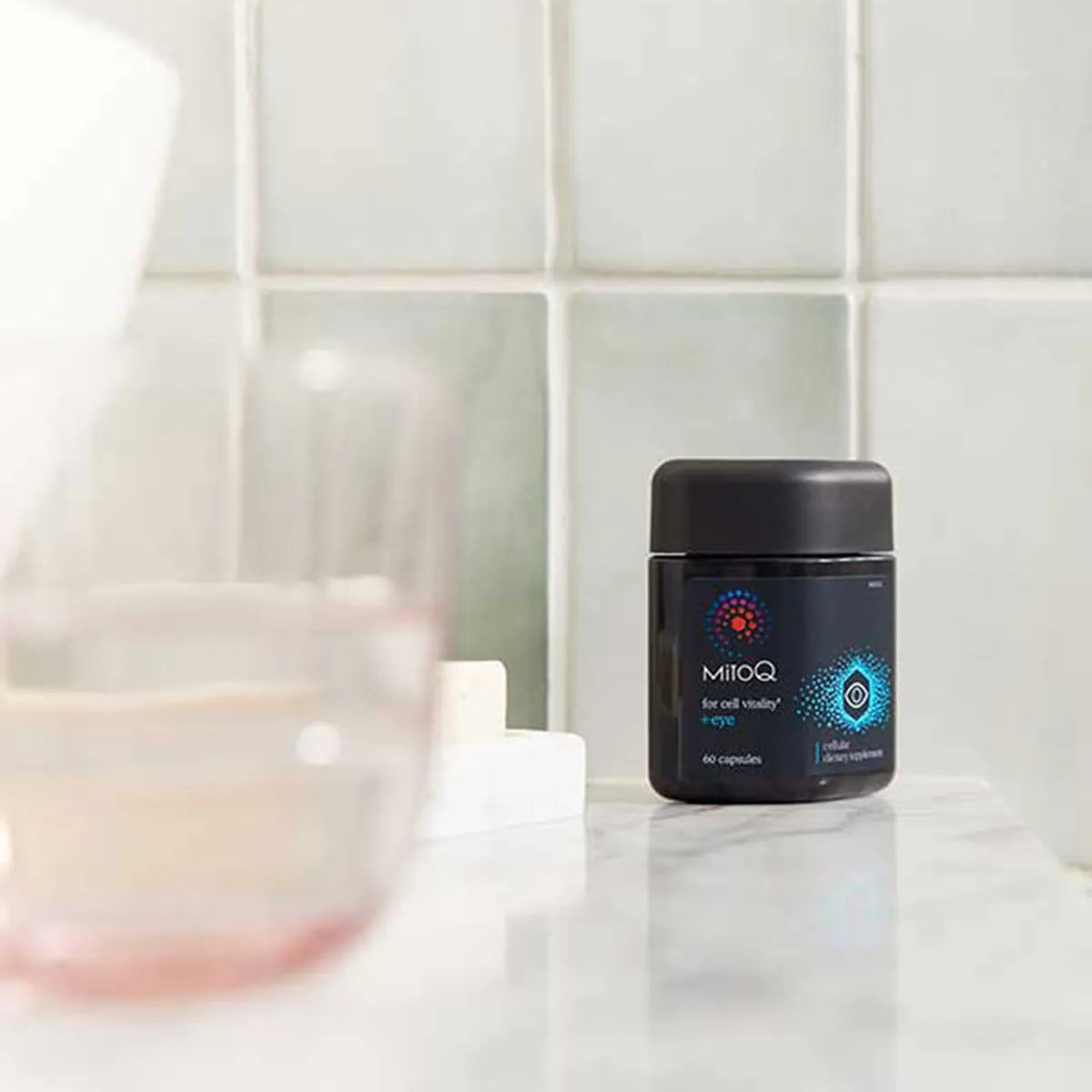 A black jar of MitoQ dietary supplement capsules standing on a marble countertop in a bathroom setting.