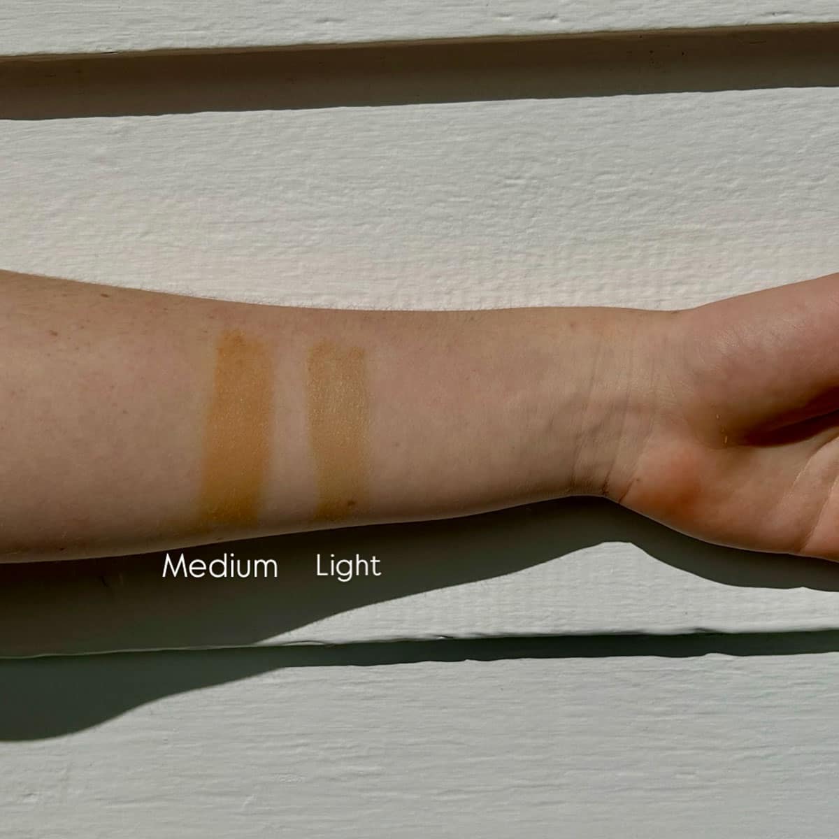 Swatches of 'Medium' and 'Light' makeup on a person's arm against a neutral background.