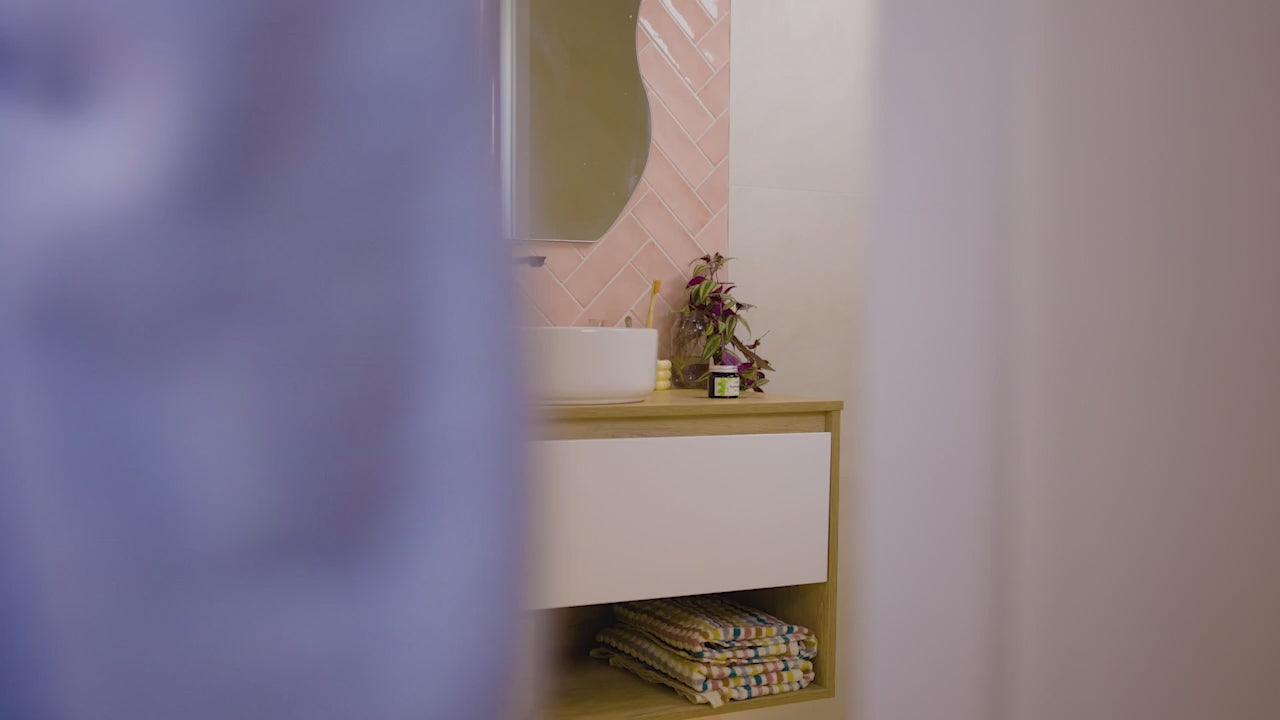 Person using solid toothpaste from a jar in a bathroom.