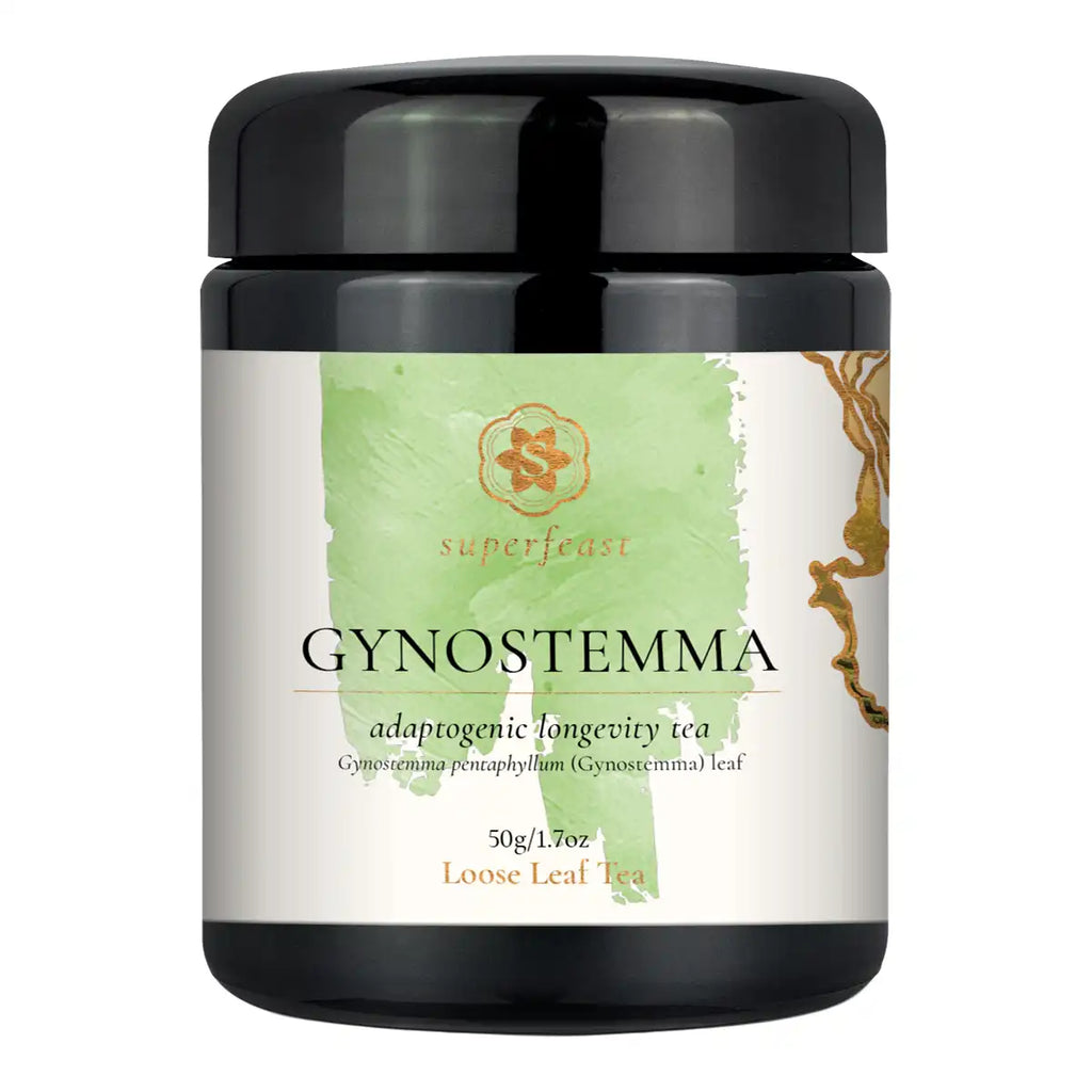 A black jar of SuperFeast Gynostemma adaptogenic longevity tea, featuring a white label with a light green watercolor design and gold accents.