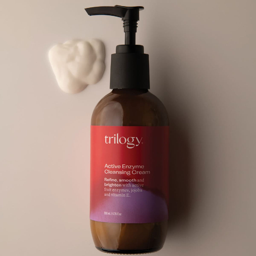 Brown bottle of Trilogy Active Enzyme Cleansing Cream with a pump on a beige background.