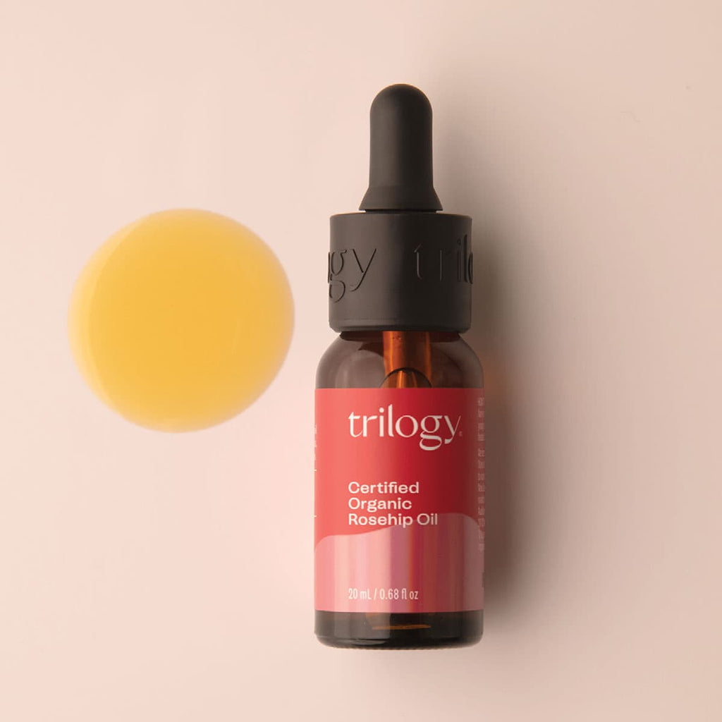 Bottle of Trilogy Certified Organic Rosehip Oil with a dropper on a beige background.